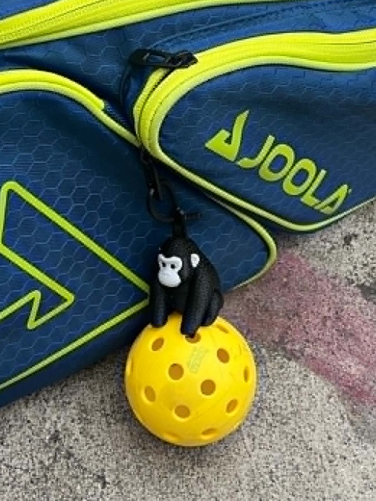 Black gorilla Pickle Palz™ charm clipped to a JOOLA pickleball bag, sitting on a yellow pickleball